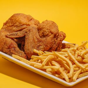 A classic platter of crispy fried chicken and golden French fries on a yellow background.
