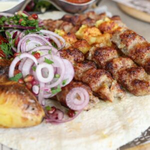 Close-up of grilled meat and vegetables served on flatbread, garnished with fresh herbs and onions.