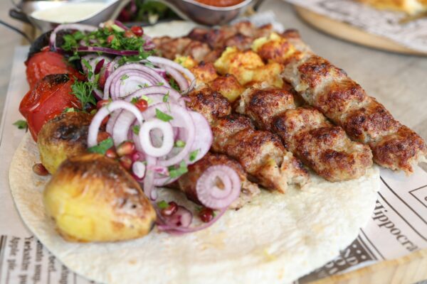 Close-up of grilled meat and vegetables served on flatbread, garnished with fresh herbs and onions.