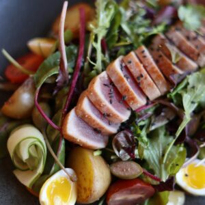 Close-up of a vibrant tuna salad with mixed greens and fresh vegetables on a black plate.