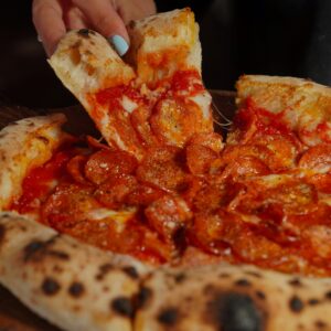 Delicious pepperoni pizza slice being lifted from a wood-fired pie with melted cheese.