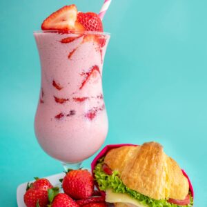 Delicious strawberry milkshake and sandwich served on a colorful background.