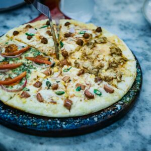 Close-up of a sliced pizza with diverse toppings on a round platter, ready to serve.