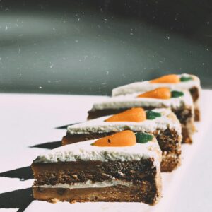 Close-up of carrot cake slices topped with cream cheese frosting and marzipan carrots on a white plate.