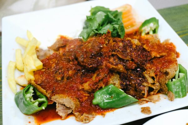 Delicious Iskender Kebab served with green peppers, fries, and tomato sauce.