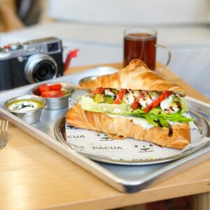 Artistic shot of a gourmet croissant sandwich paired with a vintage camera in a cozy café setting.