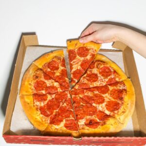 Close-up of a hand picking a slice of tasty pepperoni pizza from a box.