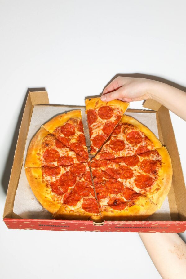 Close-up of a hand picking a slice of tasty pepperoni pizza from a box.