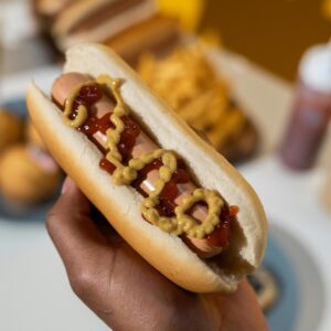 A hot dog covered in mustard and ketchup held against a colorful background.