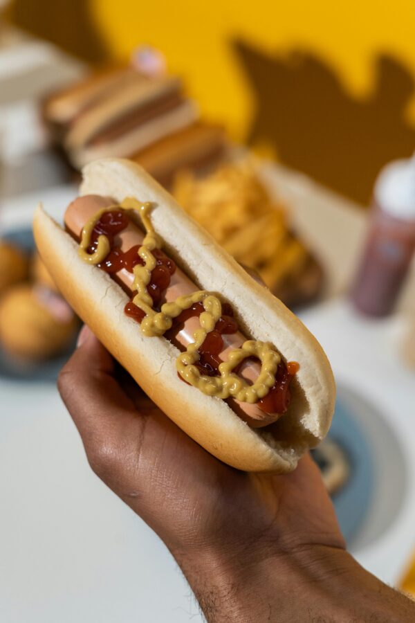 A hot dog covered in mustard and ketchup held against a colorful background.