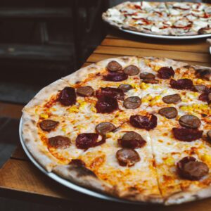 Close-up of a delicious pizza with sausage, corn, and cheese on an outdoor table.