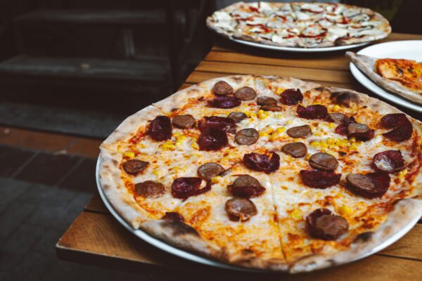 Close-up of a delicious pizza with sausage, corn, and cheese on an outdoor table.