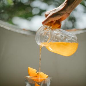 Hand pouring fresh orange juice into a glass, capturing a vibrant summer moment.