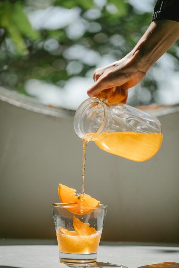 Hand pouring fresh orange juice into a glass, capturing a vibrant summer moment.