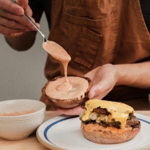 Person preparing a tasty homemade cheeseburger with sauce in a kitchen setting.